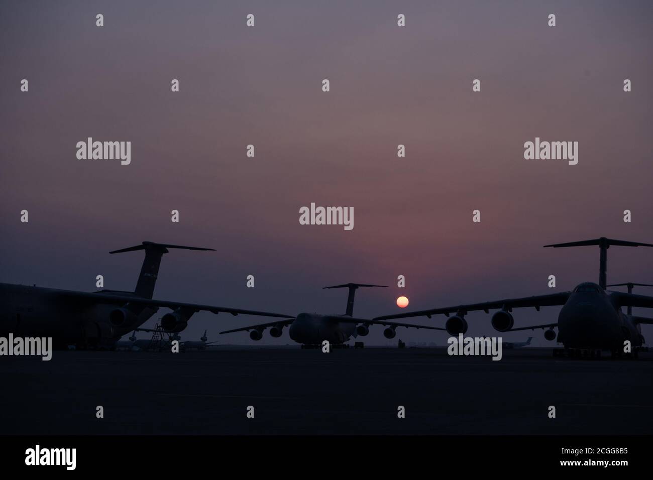 The sun rises behind C-5M Super Galaxies parked at Travis Air Force Base, California, Aug. 28, 2020. The C-5M, with a cargo load of 281,001 pounds, can fly 2,150 nautical miles, offload, and fly to a second base 500 nautical miles away from the original destination — all without aerial refueling. (U.S. Air Force photo by Nicholas Pilch) Stock Photo