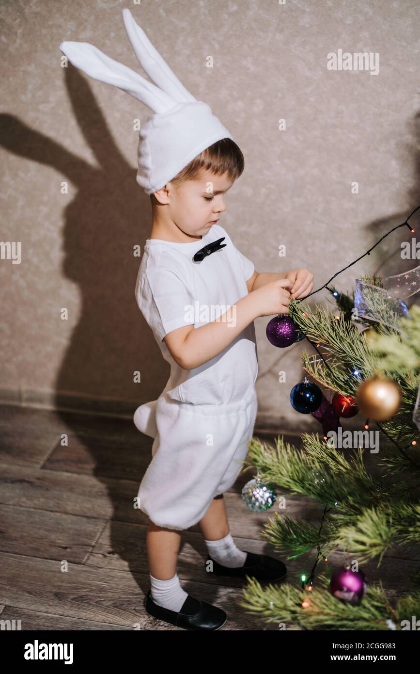 Celebrating Christmas. A cute baby in a bunny or rabbit costume decorates the Christmas tree with New Year s toys Stock Photo Alamy