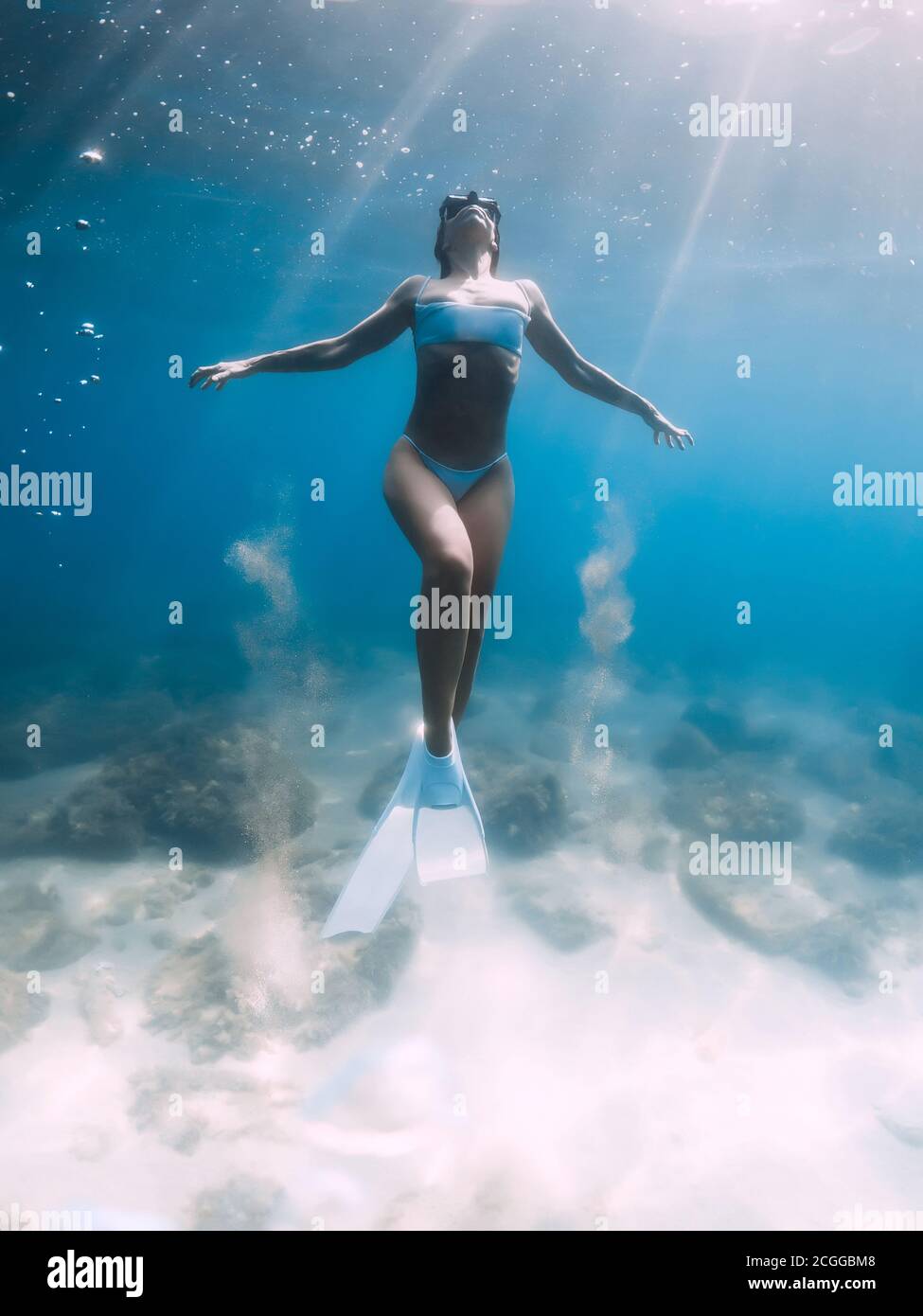 Freediver girl glides and posing over sandy sea with white freediving