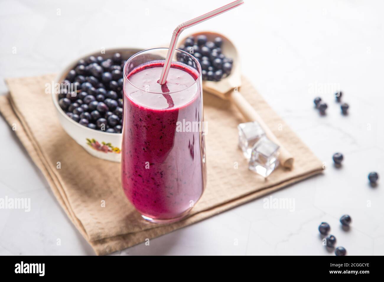 Diet drink blueberry smoothie in a glass glass with a tube, white plate with berries on a light background, with a beige napkin, in a wooden spoon-blu Stock Photo