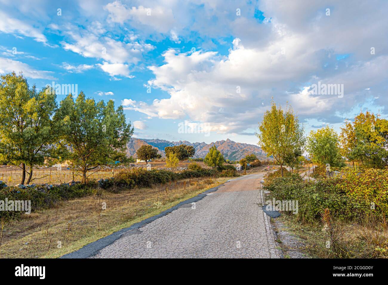 rural road surrounded by fields and in the background the Sierra de Guadarrama one day with some clouds. Madrid. Spain Stock Photo