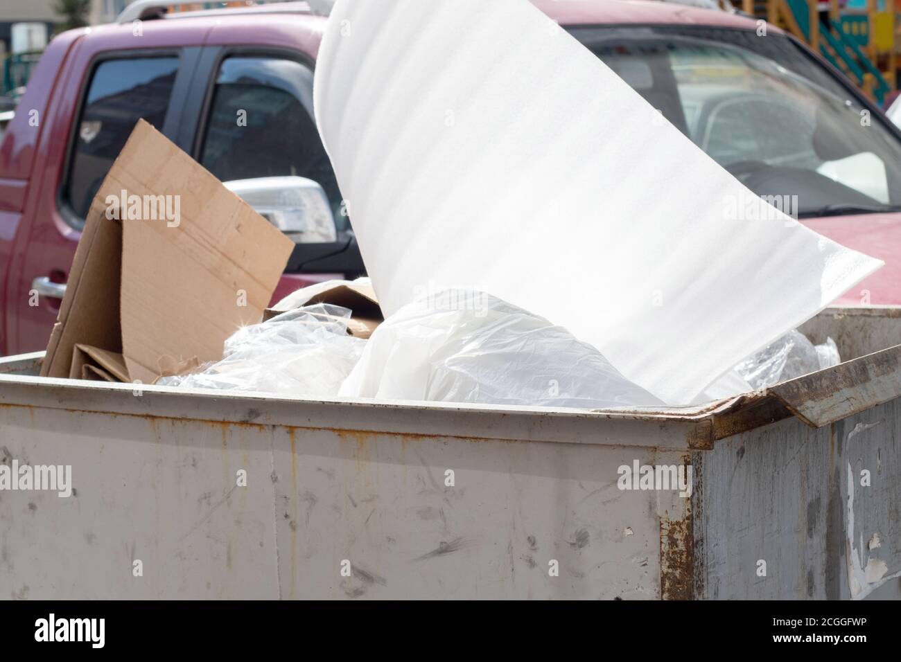 Overflowing trash can on a city street in front of a car. Plastic trash
