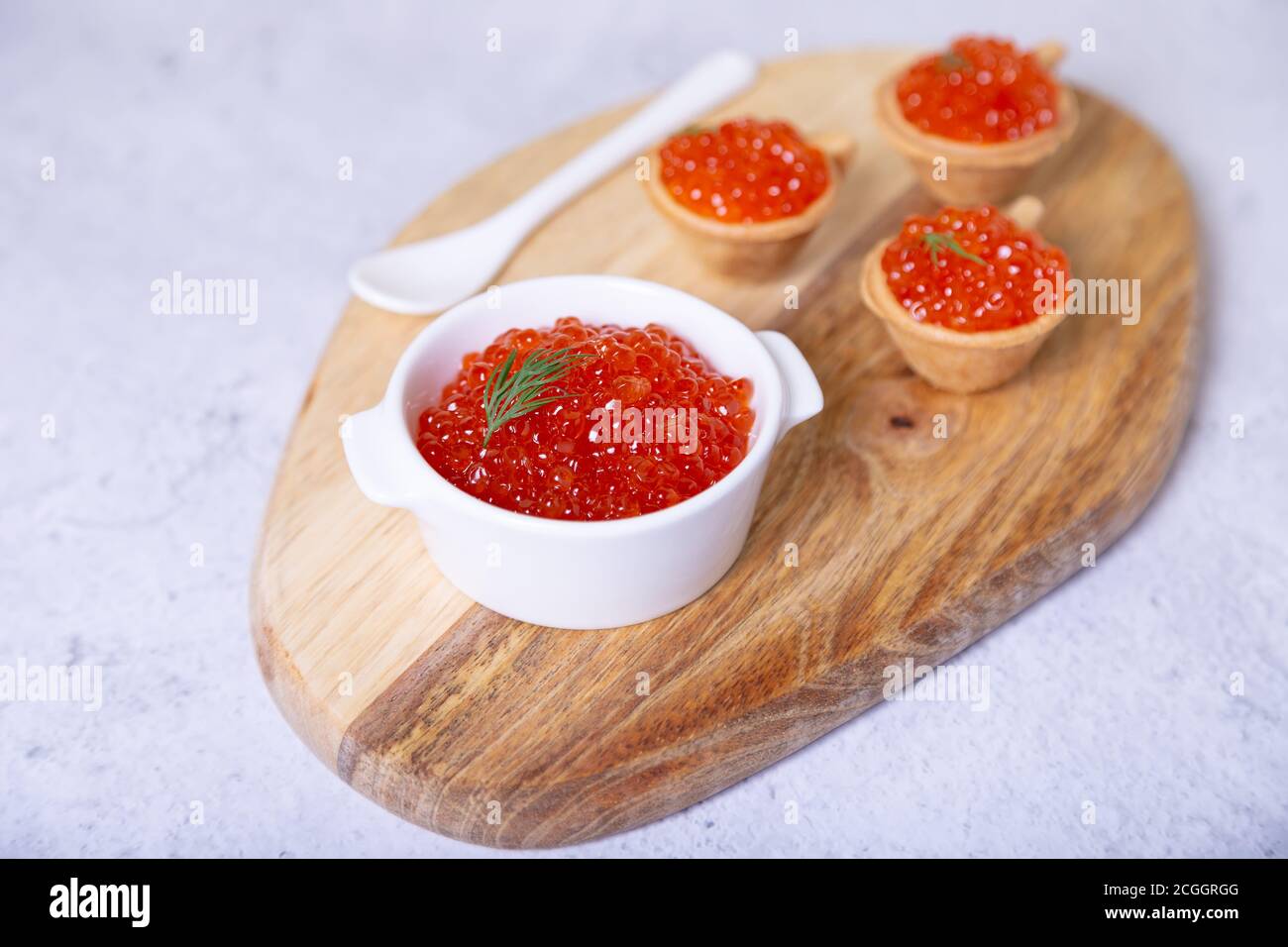 Red caviar (salmon caviar) in a white bowl on a wooden board. In the background are tartlets with caviar. Selective focus, close-up. Stock Photo