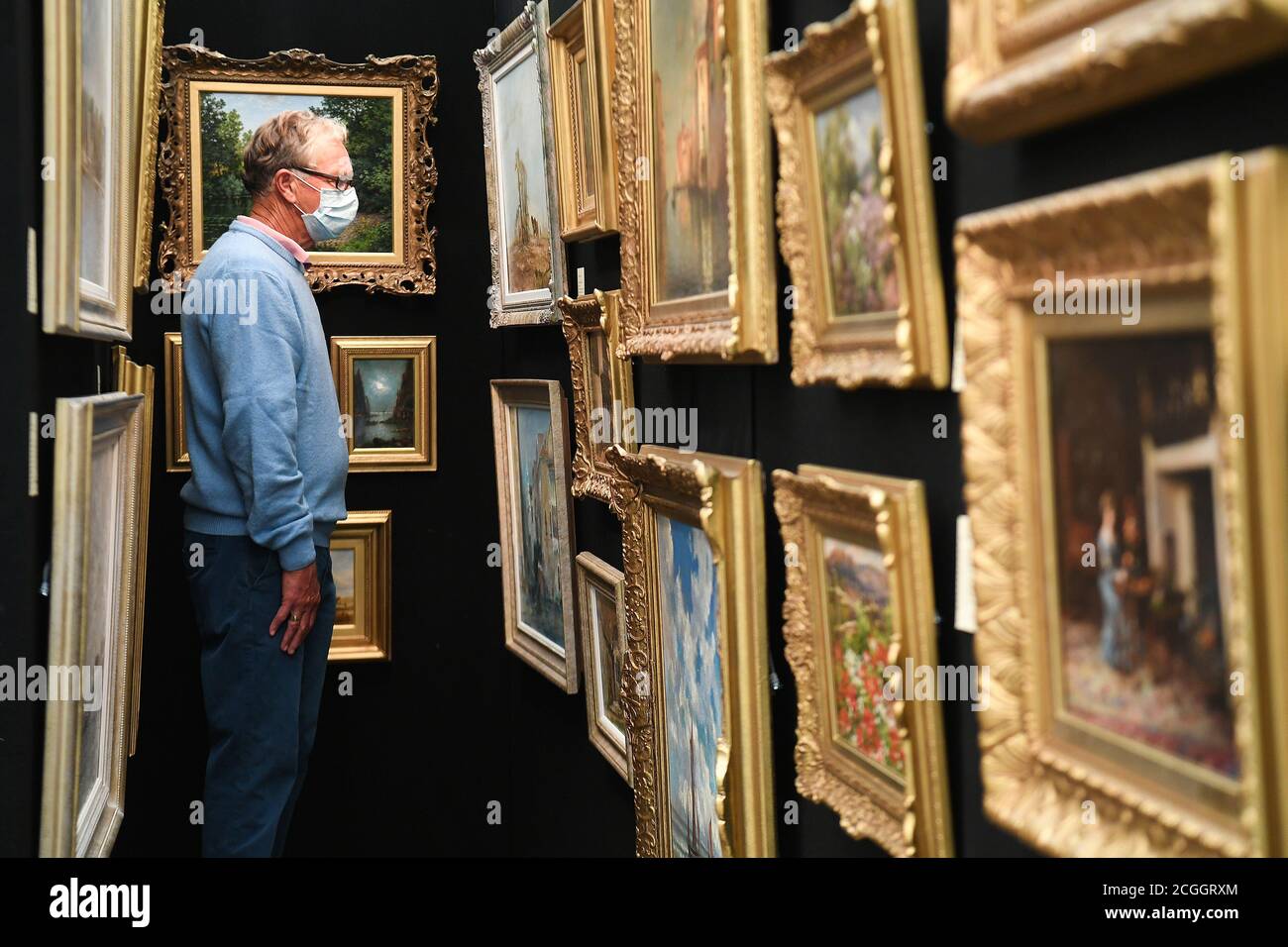 A customer looks at paintings at the Petworth Park Antiques and Fine Art Fair, at Petworth House in West Sussex. Stock Photo