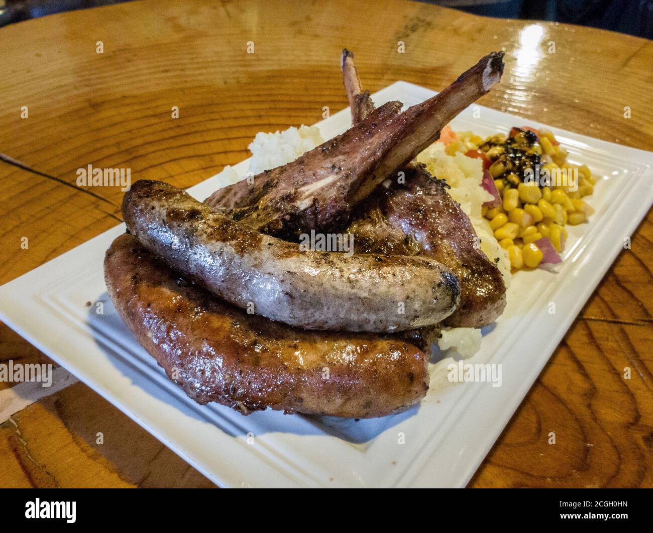 Lamb meat platter -Lamb chop, boerewors which is South African style sausage, pork banger on a plate with garlic potato, creamy spinach and slaw. Stock Photo