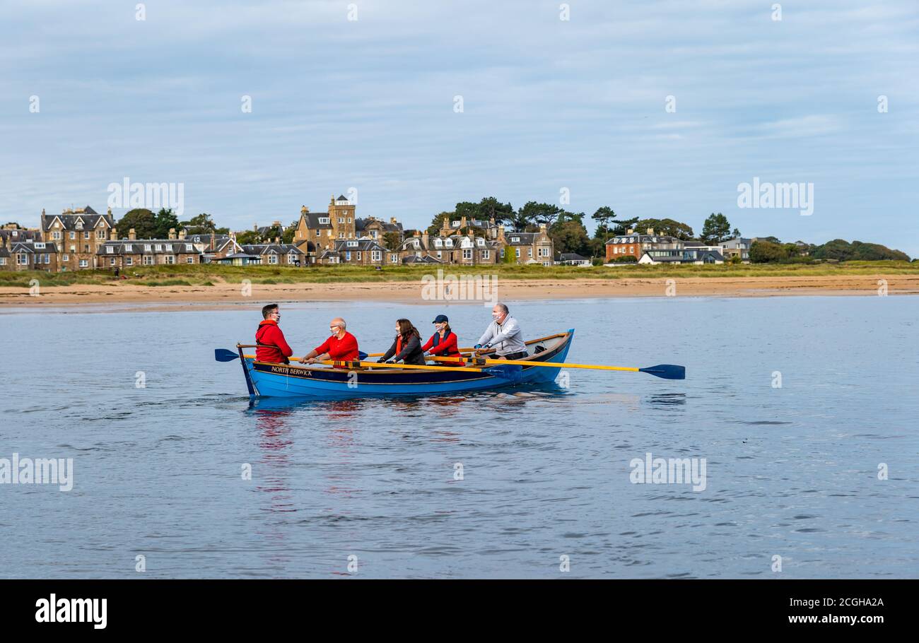 Coastal rowing crew in a St Ayle's wooden skiff wearing face masks in West Bay, North Berwick, East Lothian, Scotland, UK Stock Photo