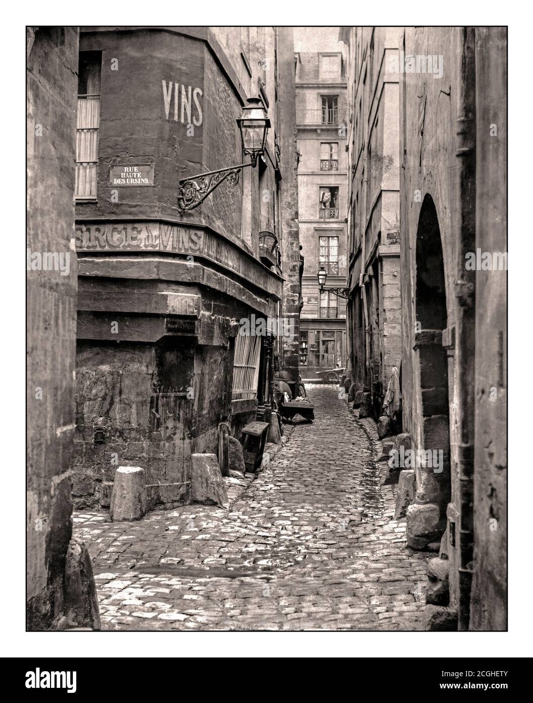 PARIS 1800’s VINTAGE B&W STREET VIEW Rue de Glatigny Paris France by Charles Marville Looking along cobbled lane with plaque on wall and VINS sign branching off on left reading: Rue Haute des Ursins, lantern in bracket on corner of building, arched doorway on right. Date 1865 Stock Photo