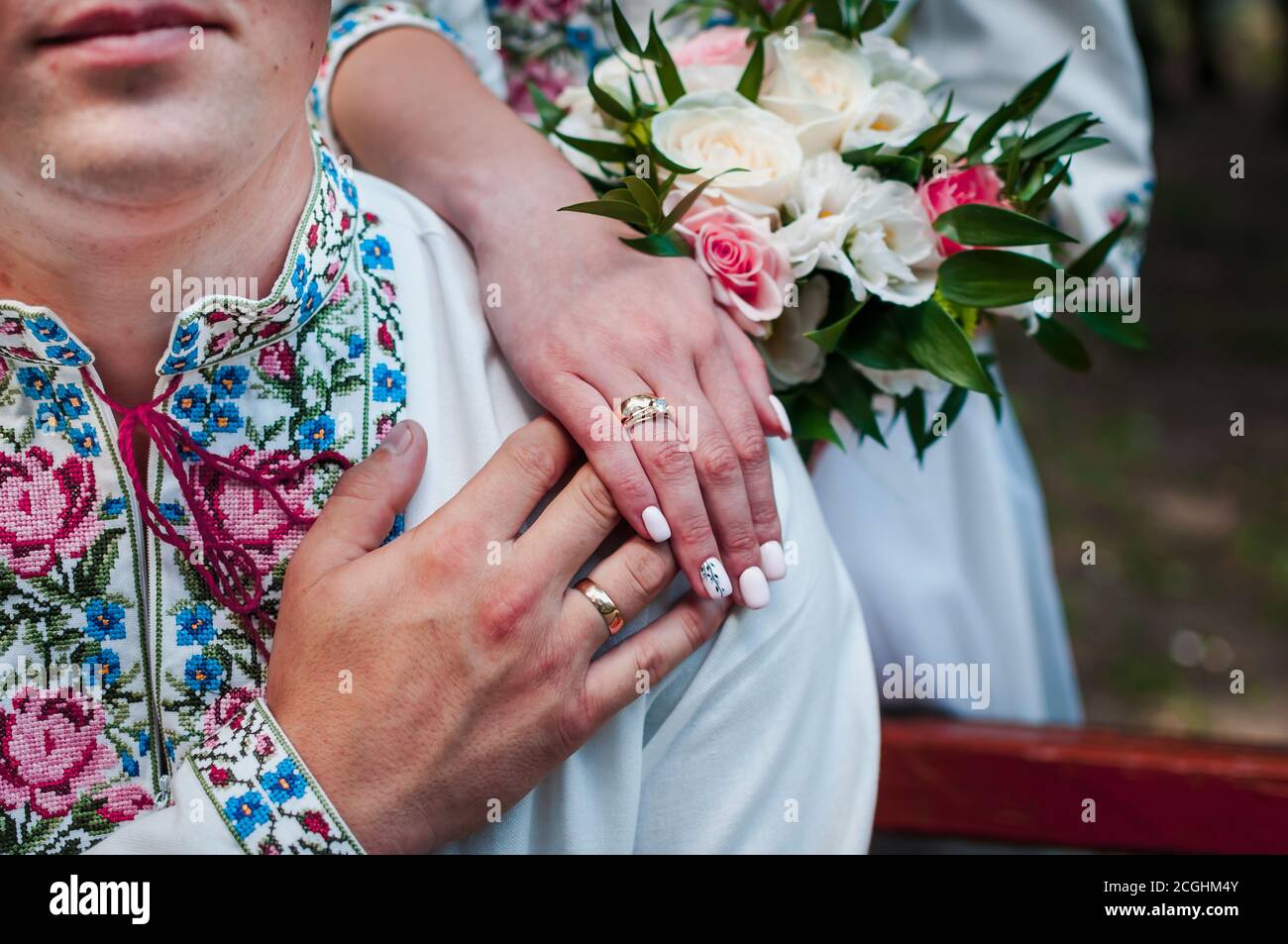 hands of newlyweds with wedding rings on a wedding bouquet with white and pink roses Stock Photo