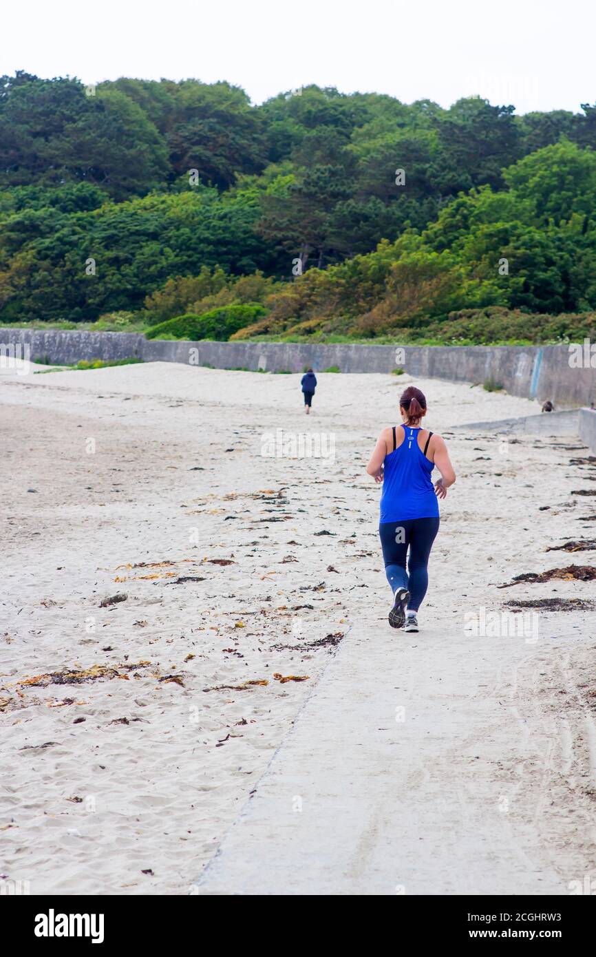 17 June 2020. Bangor County Down Northern Ireland. A female jogger wearing running gear runs the beach at Ballyholme Bay on a dull summer day. Stock Photo