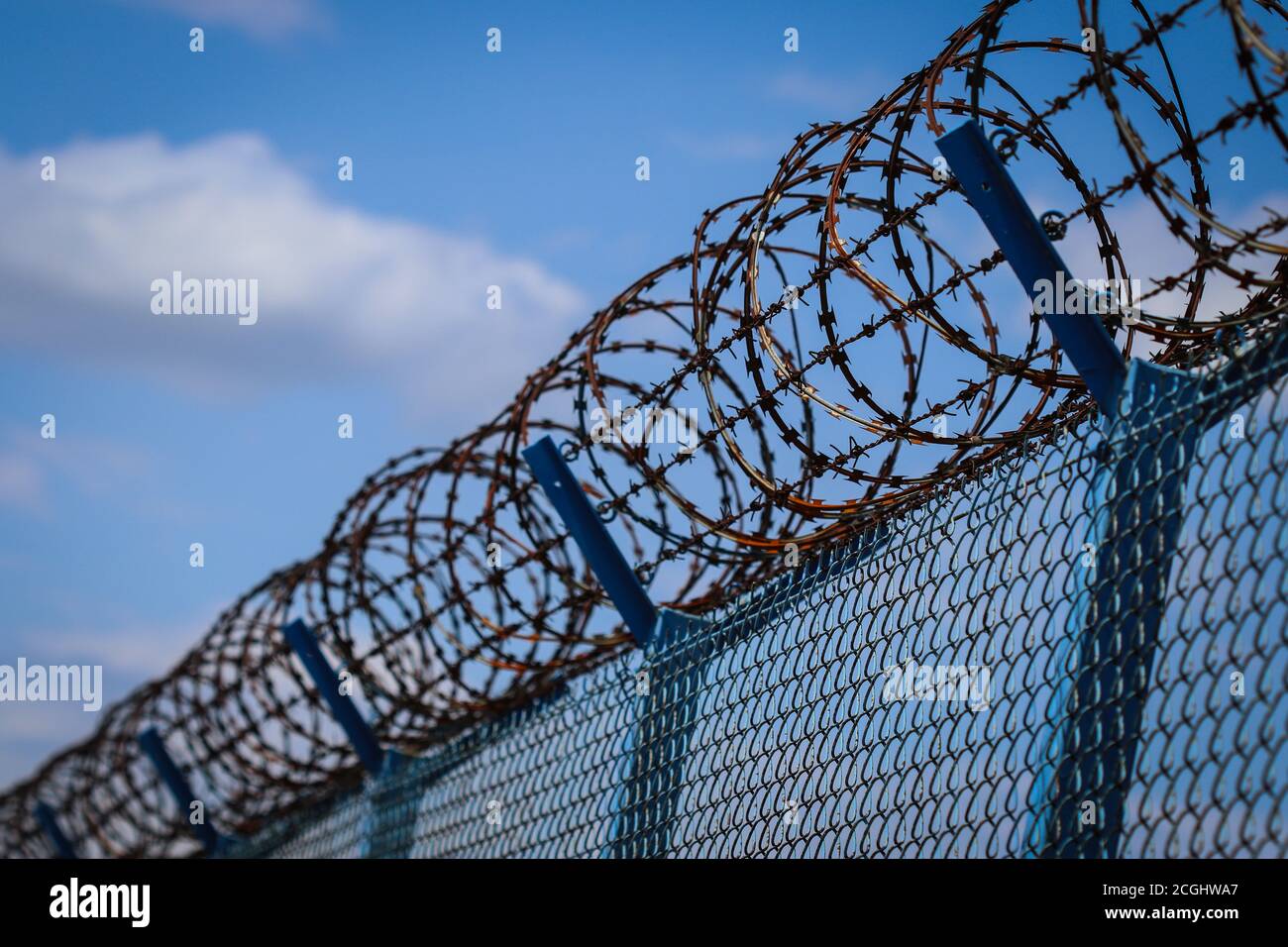 Barbed wire on top of metal mesh netting fence enclosing airport against cloudy sky Stock Photo
