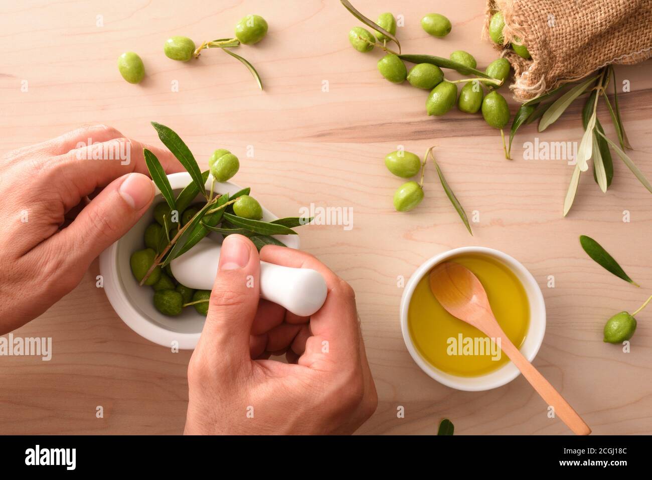 Person hands making olive oil essence with mortar for body and culinary care on table with sack of olives. Top view. Stock Photo