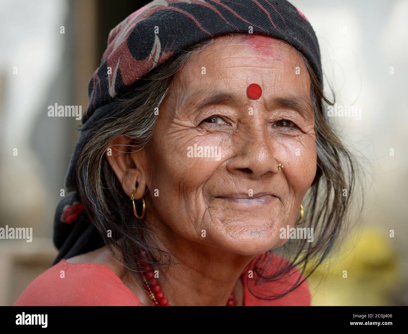 Closed-mouth smiling elderly Nepali Hindu woman with red bindi on her forehead poses for the camera. Stock Photo