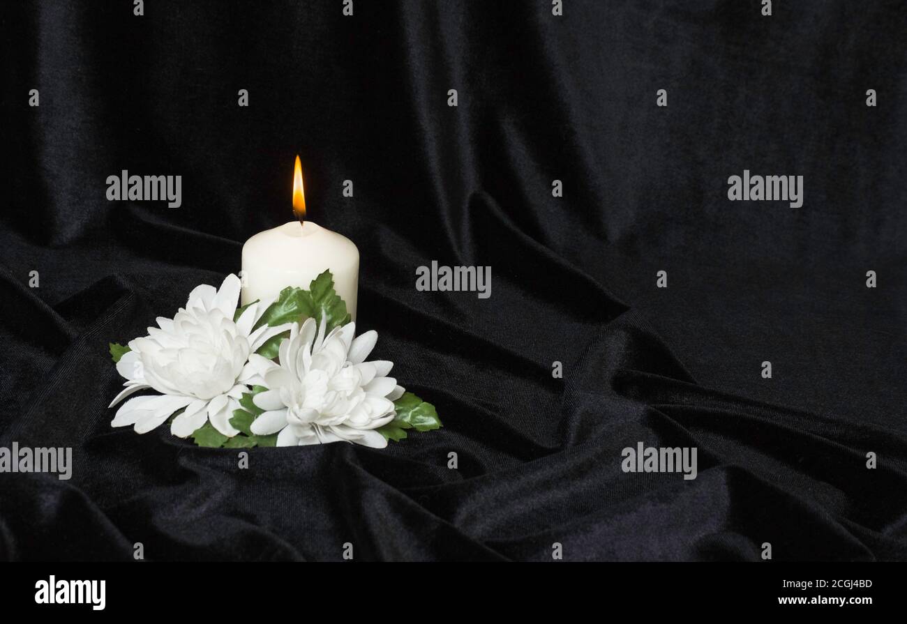 Condolence card. White burning candle and white flowers on a black background, free space for