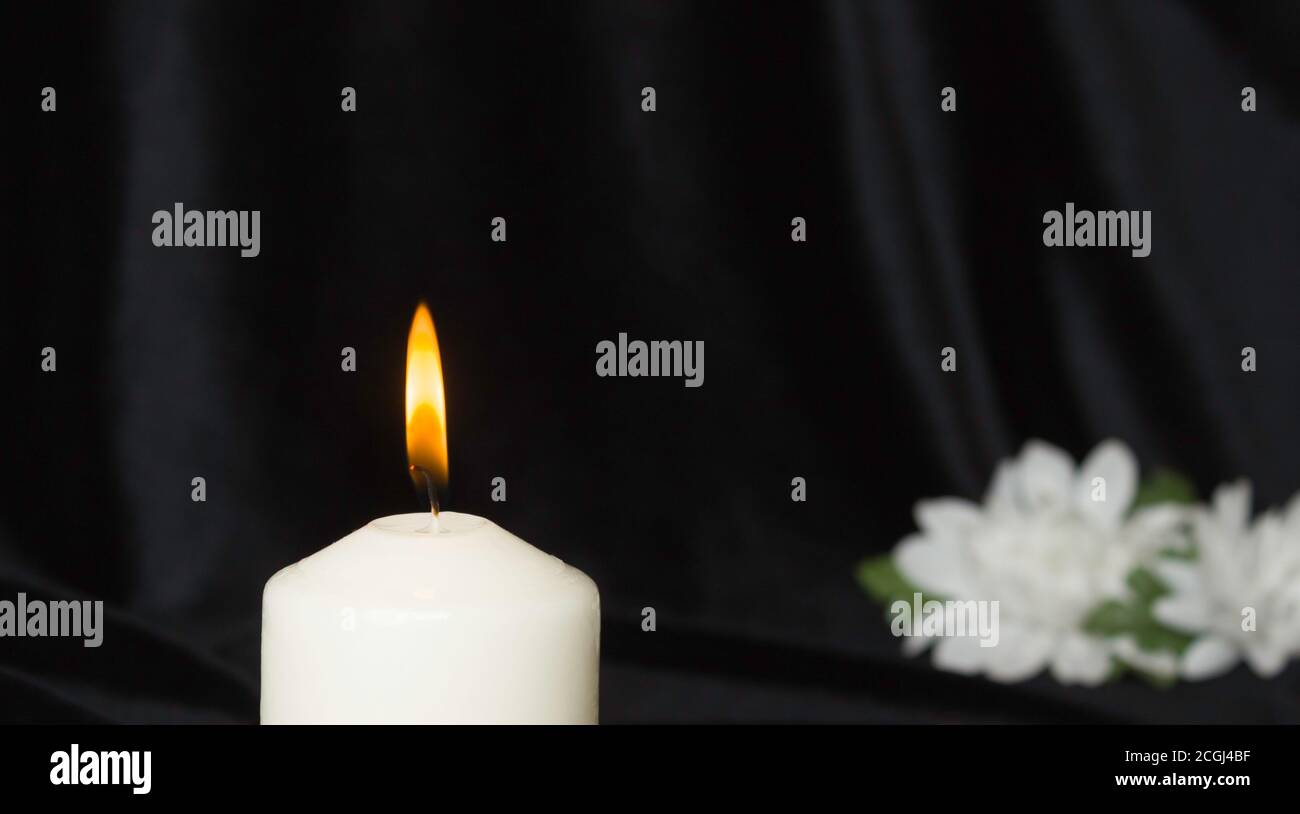 Condolence card. White memorial candle with white flowers in the background. Black background. Stock Photo