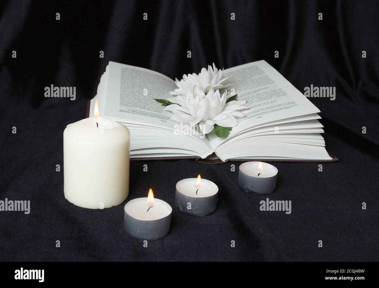 Condolence card. A white memorial candle with white flowers and an open book. The funeral, the sadness. Stock Photo