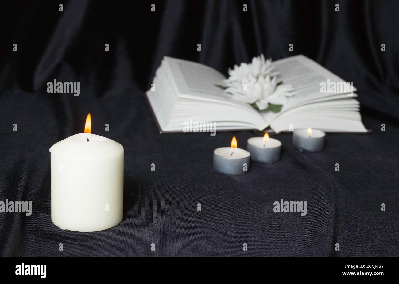 Condolence card. A white memorial candle with white flowers and an open book. The funeral, the sadness. Stock Photo