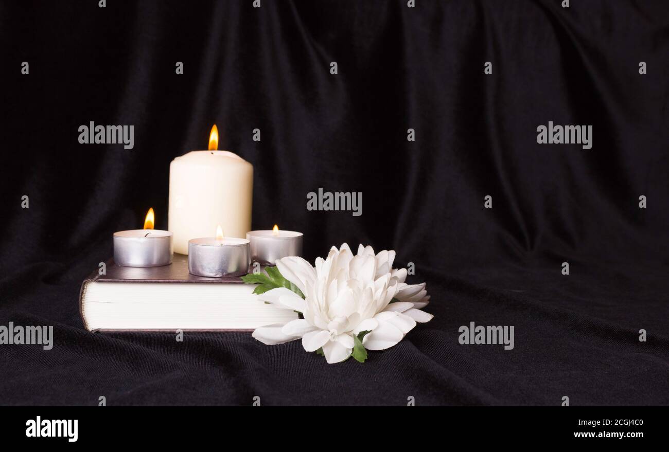 Condolence card. A white memorial candle with white flowers and book. The funeral, the sadness. Stock Photo