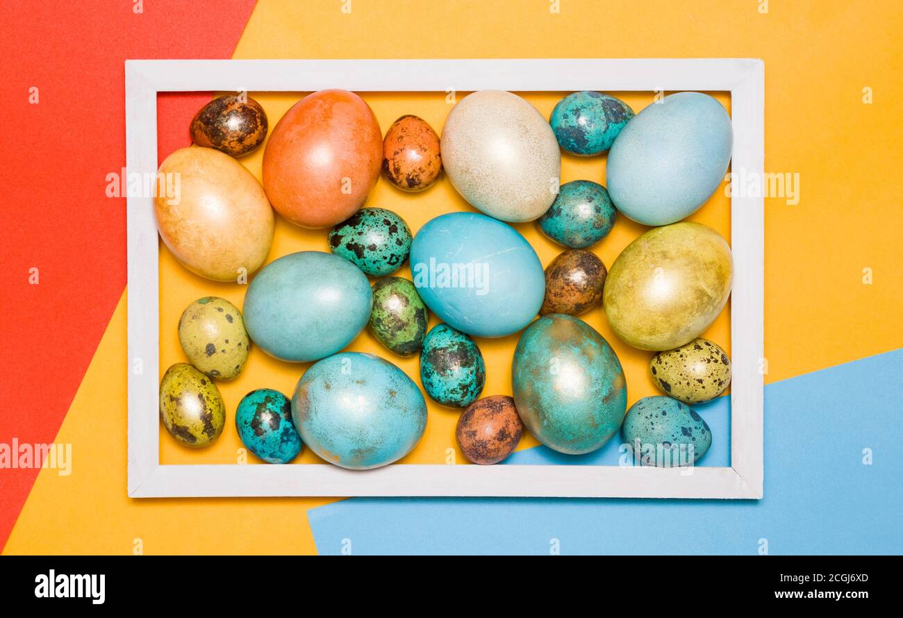 Colored Easter eggs in a wooden white frame on a colored background. Happy Easter! Stock Photo