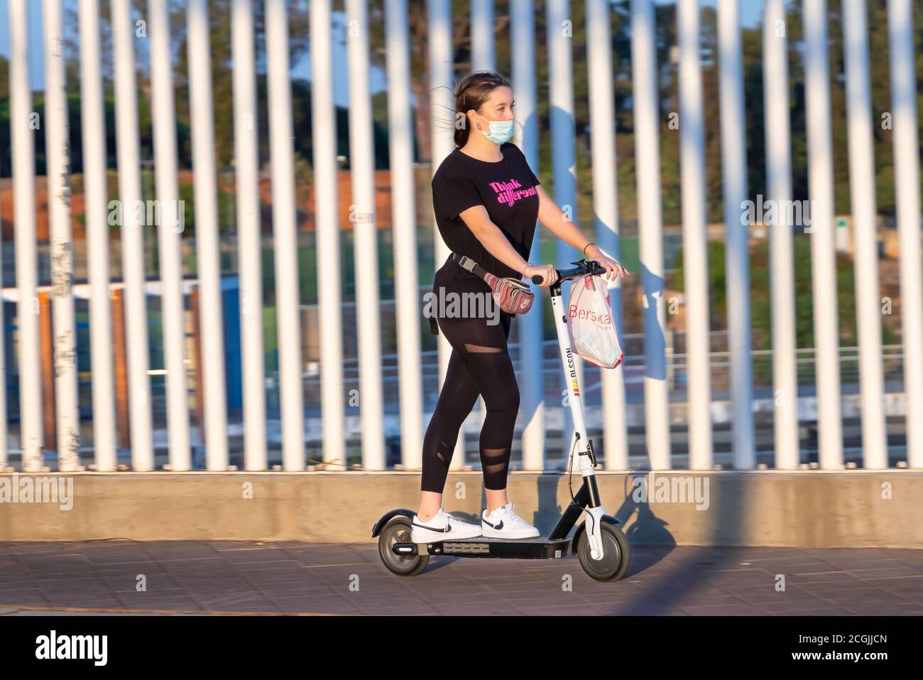 Huelva, Spain - September 10, 2020:  Young woman riding an electric scooter by the sidewalk wearing a protective mask due to coronavirus covid-19 Stock Photo