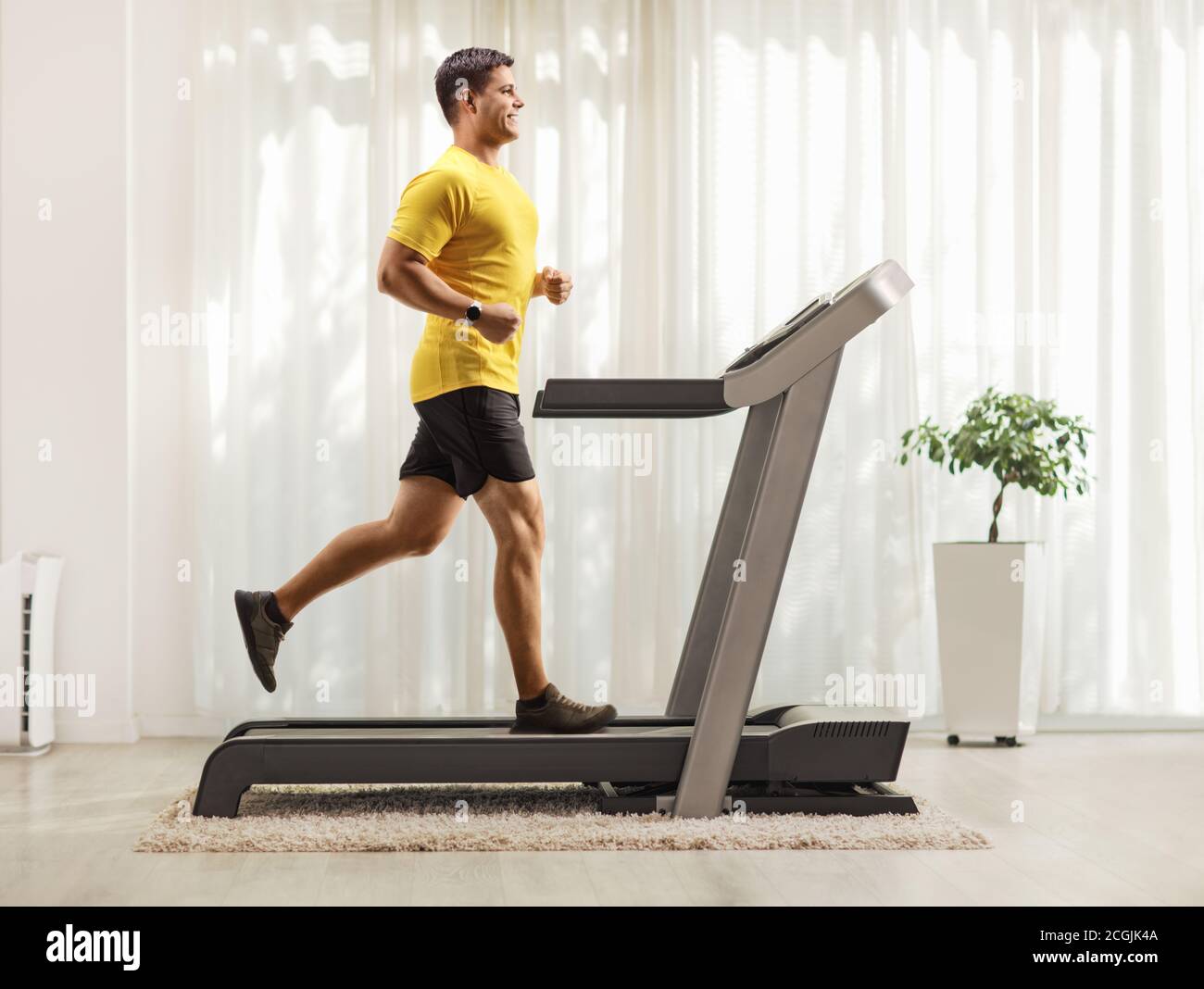 Full length profile shot of a smiling young man running on a treadmill at home Stock Photo
