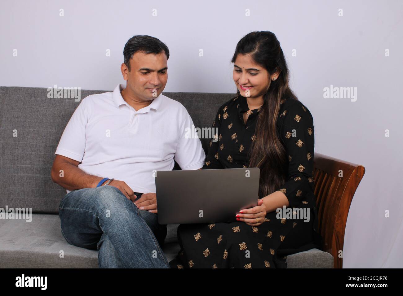 young Indian couple using the laptop sitting on a sofa. Stock Photo