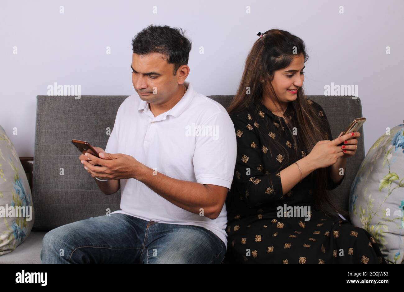 Indian couple using smartphone / mobile handset sitting on sofa Stock ...