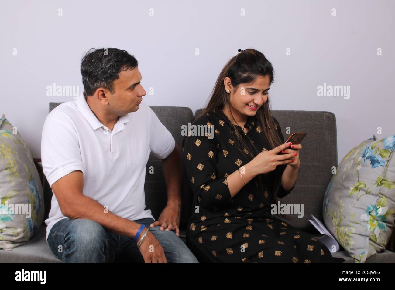 Angry indian husband looking at his wife watching her phone. Stock Photo