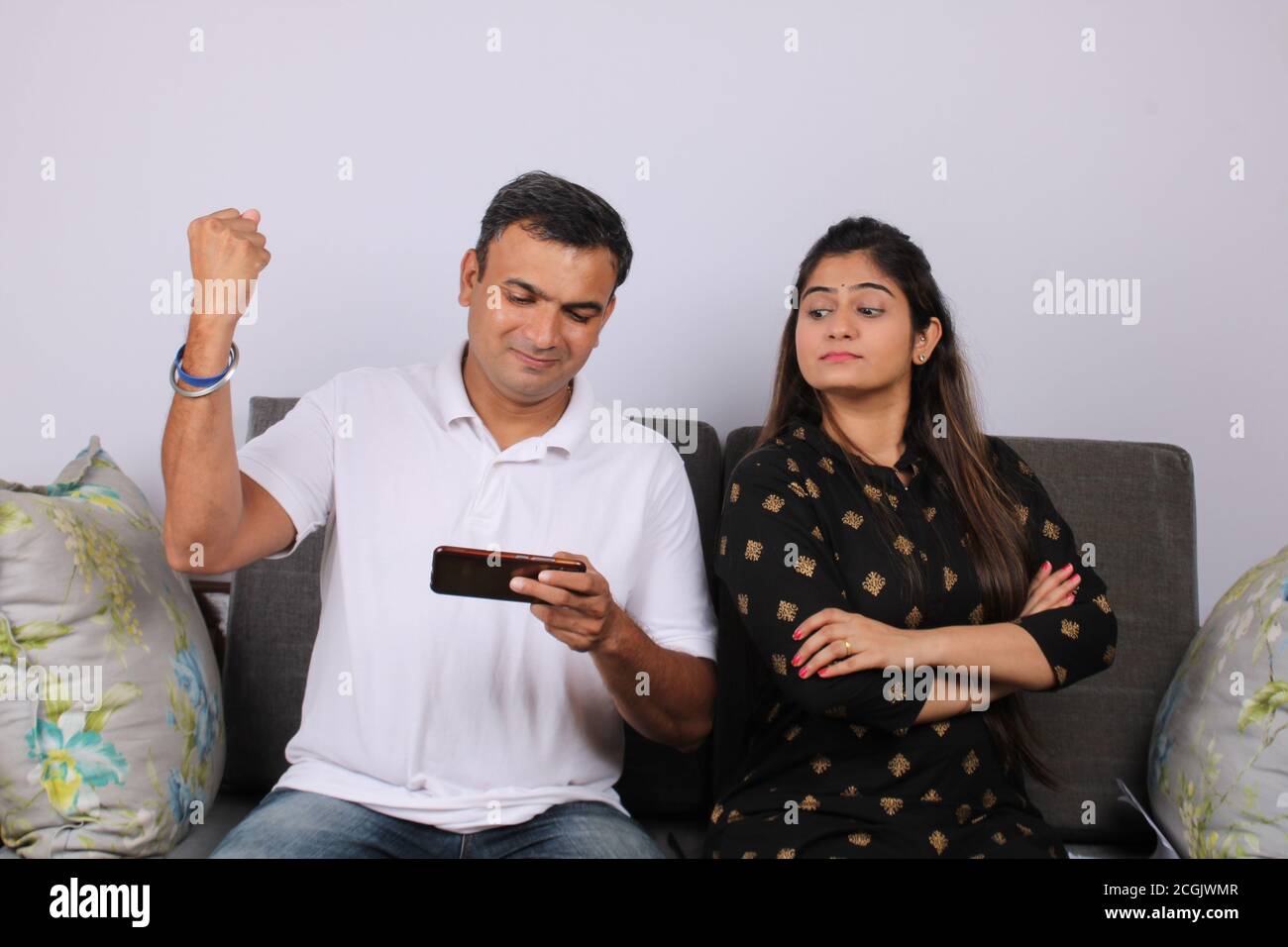 Young girl sitting on sofa is feeling bored with her husband because his addicted cellphone behavior ignoring her in relationship domestic problem. Stock Photo