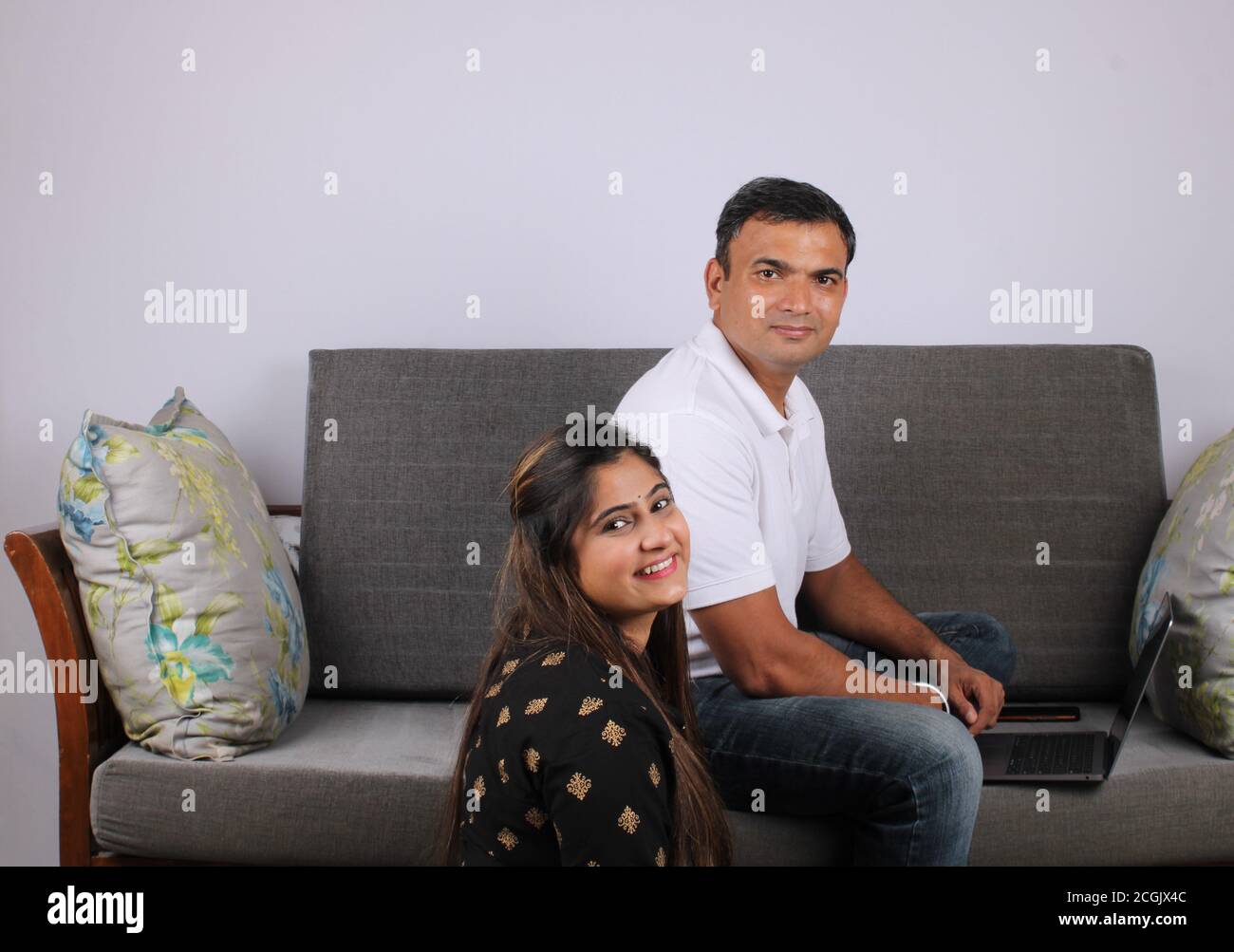 young Indian couple using the laptop sitting on a sofa. Stock Photo