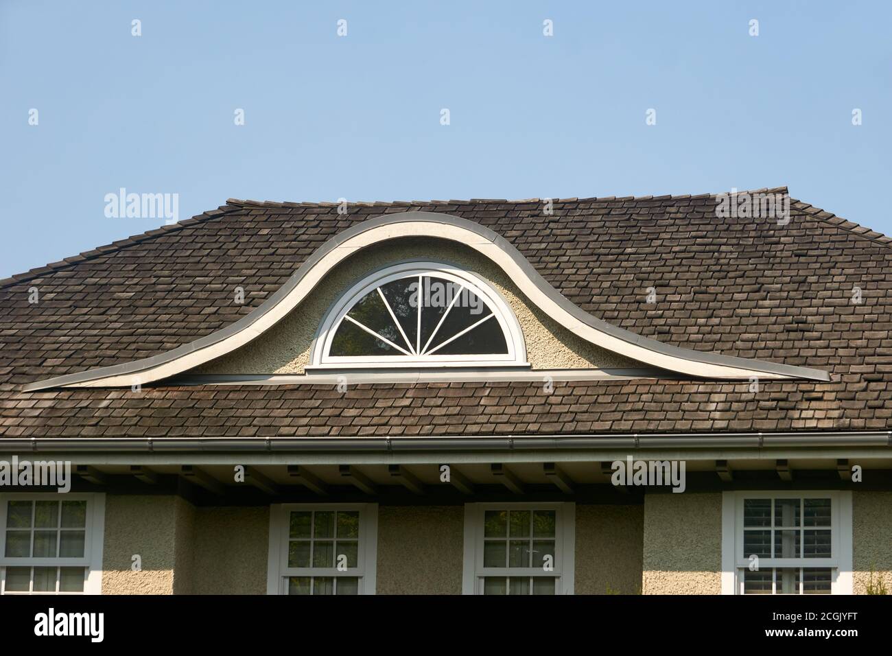 Semicircular arched attic window or eyebrow dormer in a cedar shake roof of a house Stock Photo