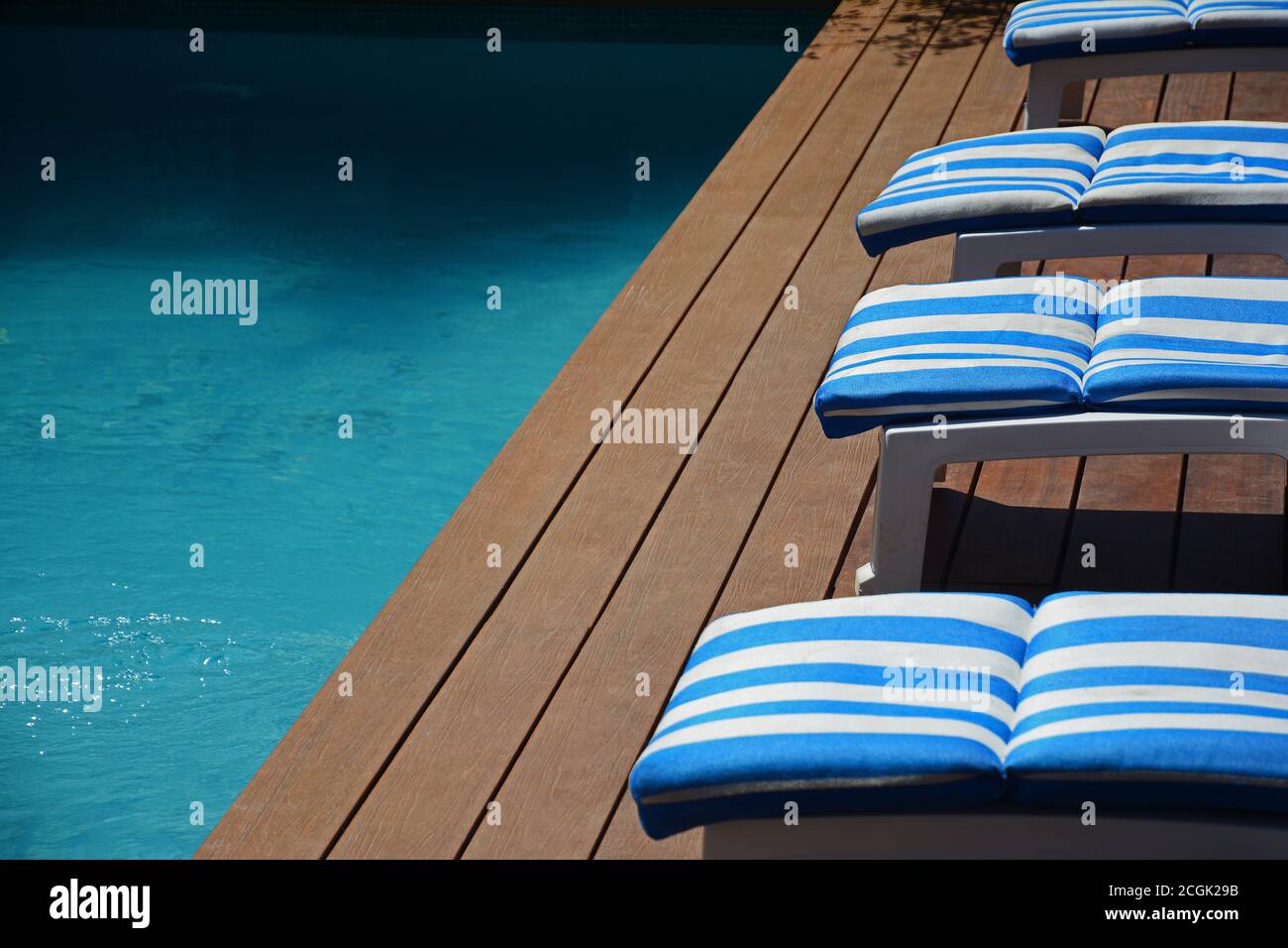Four blue and white pool deck chairs on wooden deck with partial