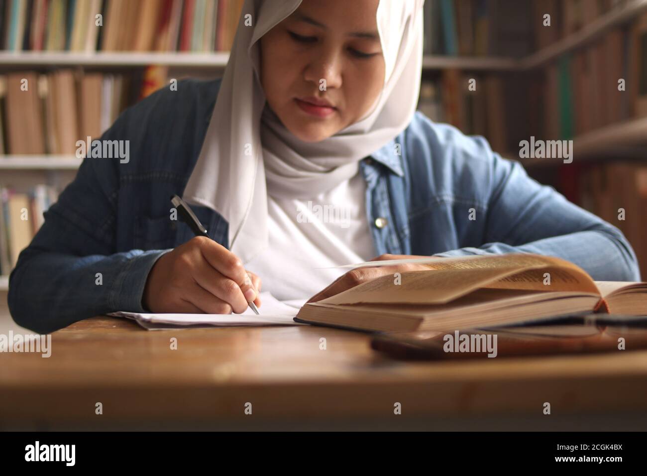Asian muslim woman studying learning in library, exam preparation concept. Female college student doing research and making notes in her book Stock Photo