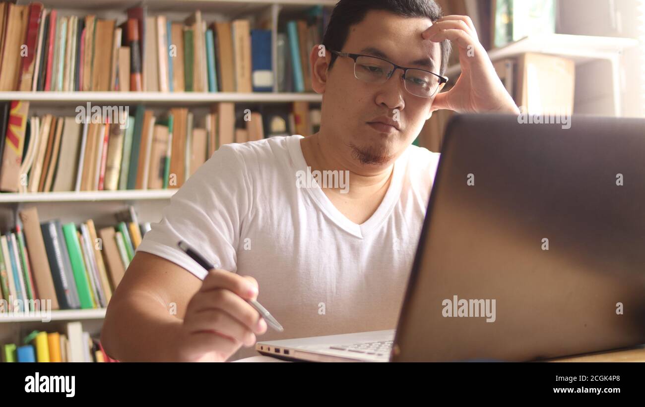 Asian muslim man studying in library, exam preparation concept. Male college student doing research and using laptop to learn online Stock Photo