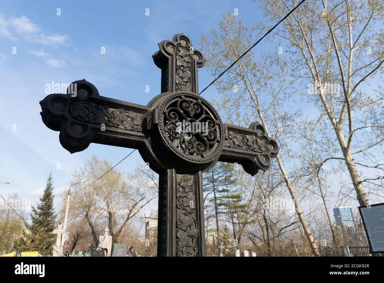 Ancient black iron forged cross banked among the sky in the Troitskoye cemetery (1842) of Krasnoyarsk city, in the spring. Stock Photo
