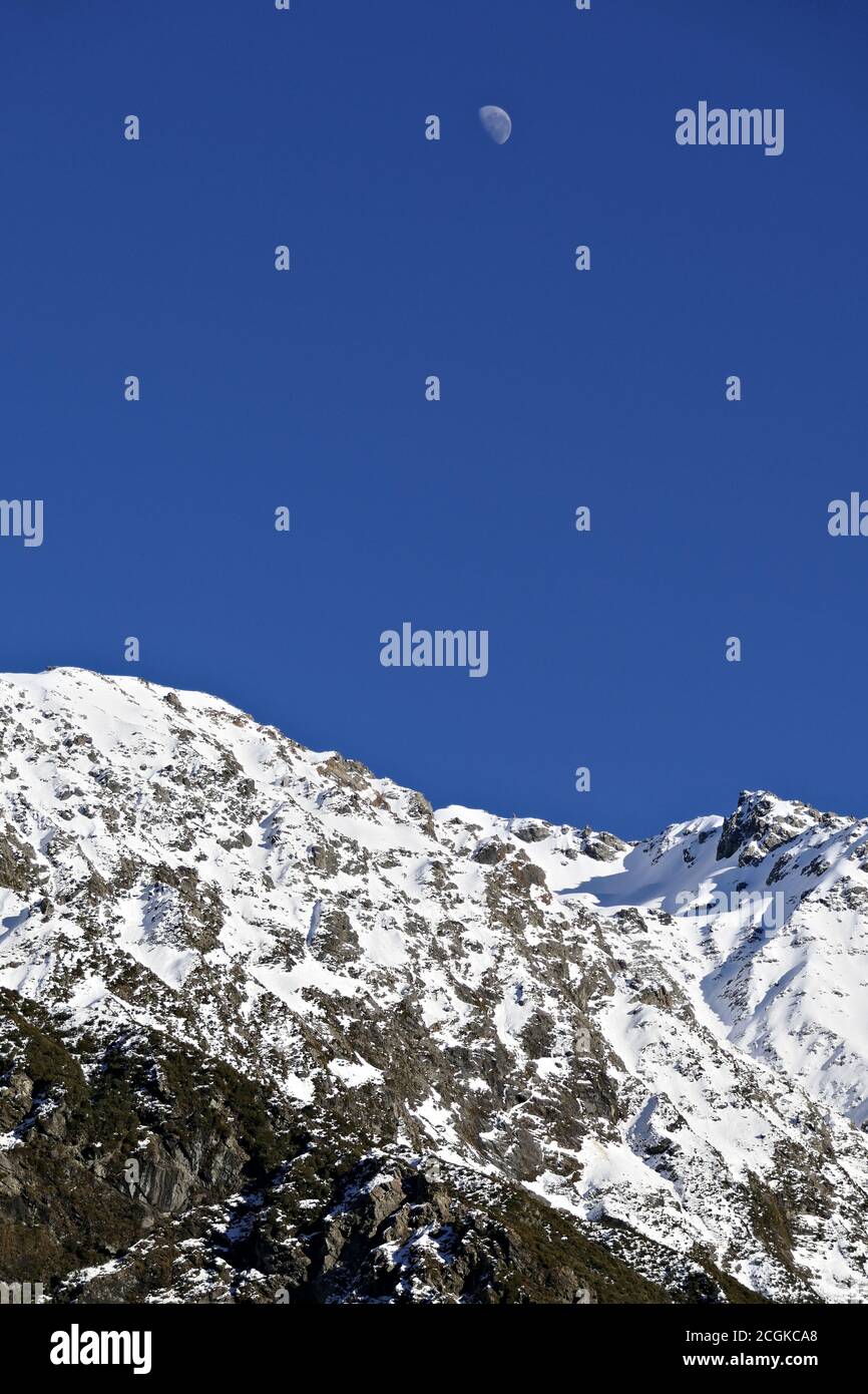Moon over scenic snow covered Alps with blue sky Stock Photo