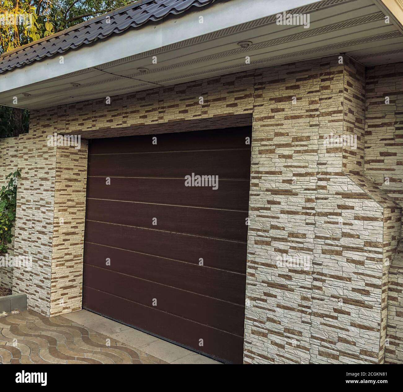 Automatic and convenient garage doors opening for a car with wall decore. Modern, plastic automatic roll-up and brown colored doorplastic, Stone Tiles Stock Photo