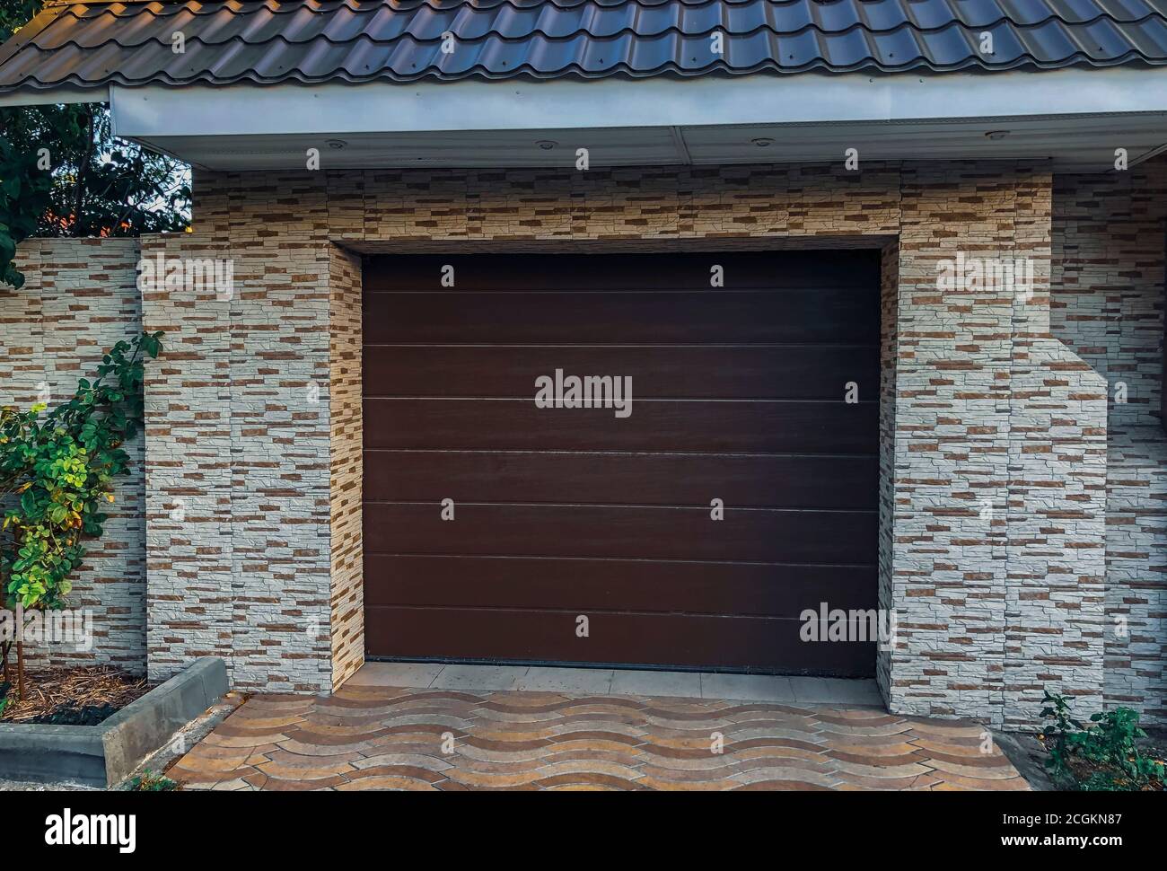Automatic and convenient garage doors opening for a car with wall decor. Modern, plastic automatic roll-up and brown colored door plastic, Stone Tiles Stock Photo