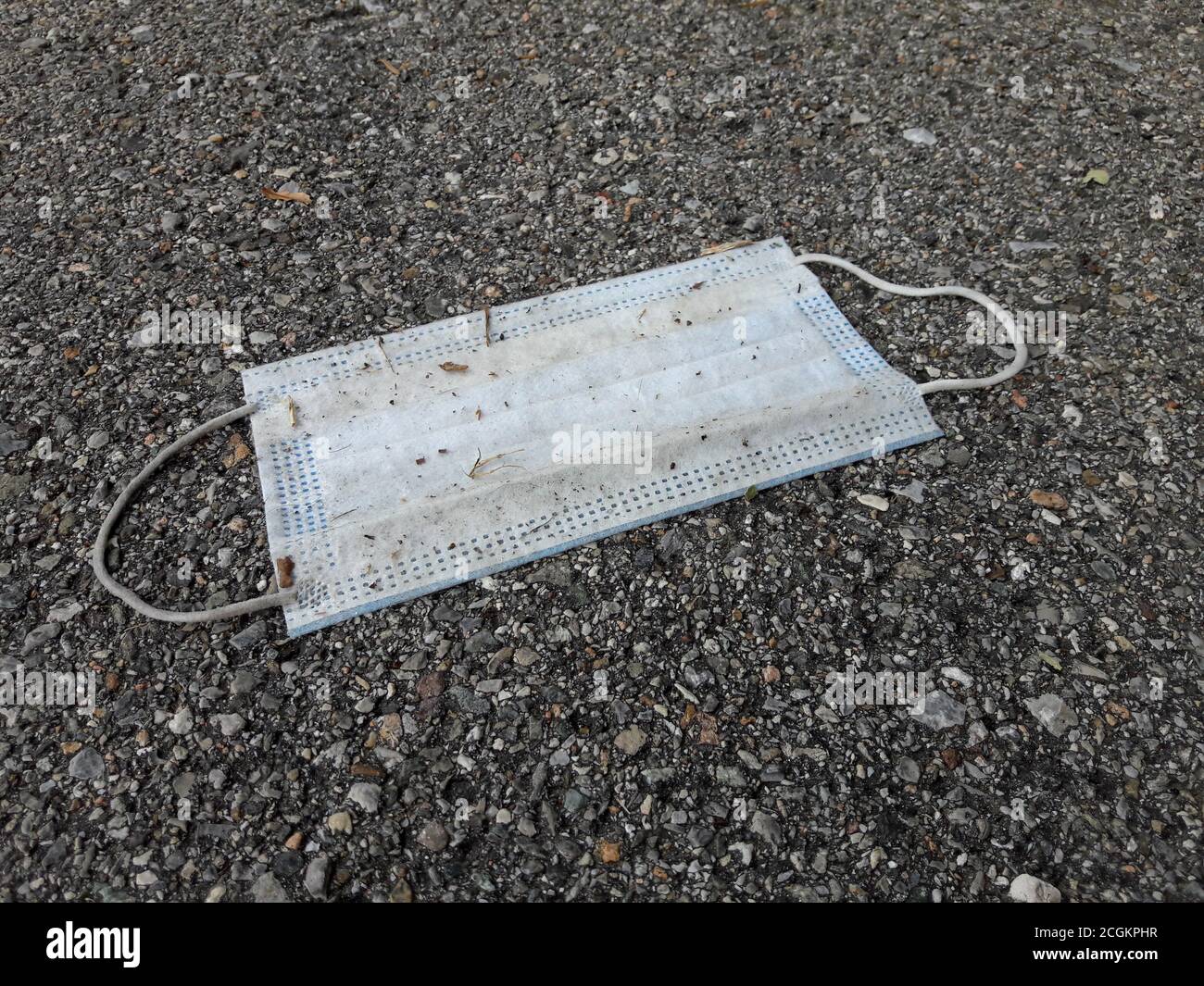 A used surgical mask dumped on a sidewalk in Switzerland. The mask are used to fight the corona virus pandemic Stock Photo