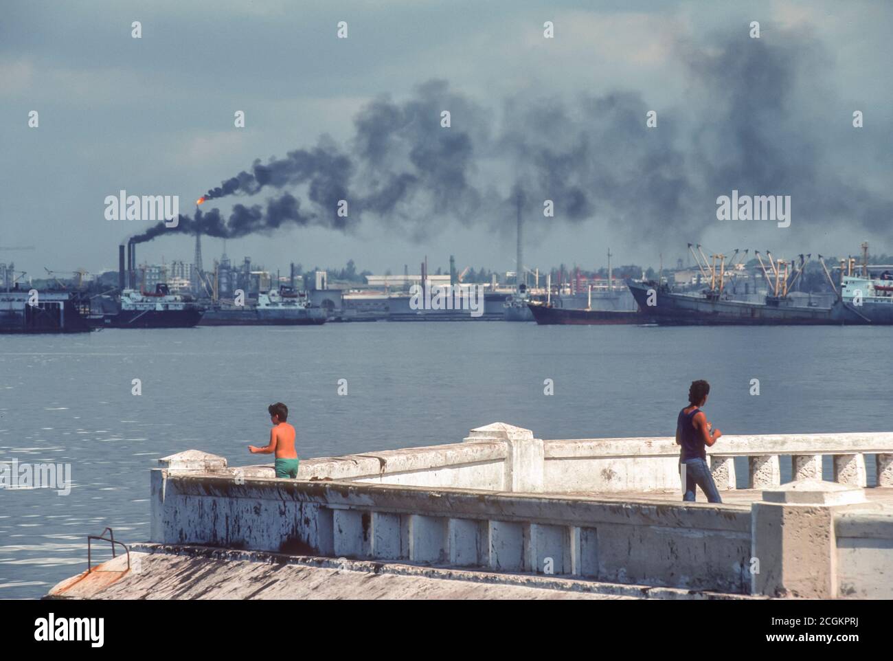 HAVANA, CUBA Two people at waterfront and oil refinery smoke and