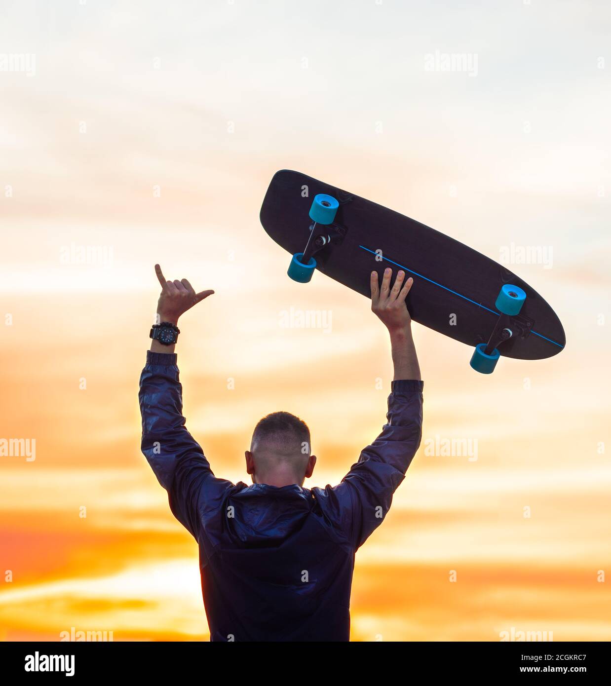 Man enjoying carefree life on sunset. Holds skateboard and showing shaka  sign Stock Photo - Alamy