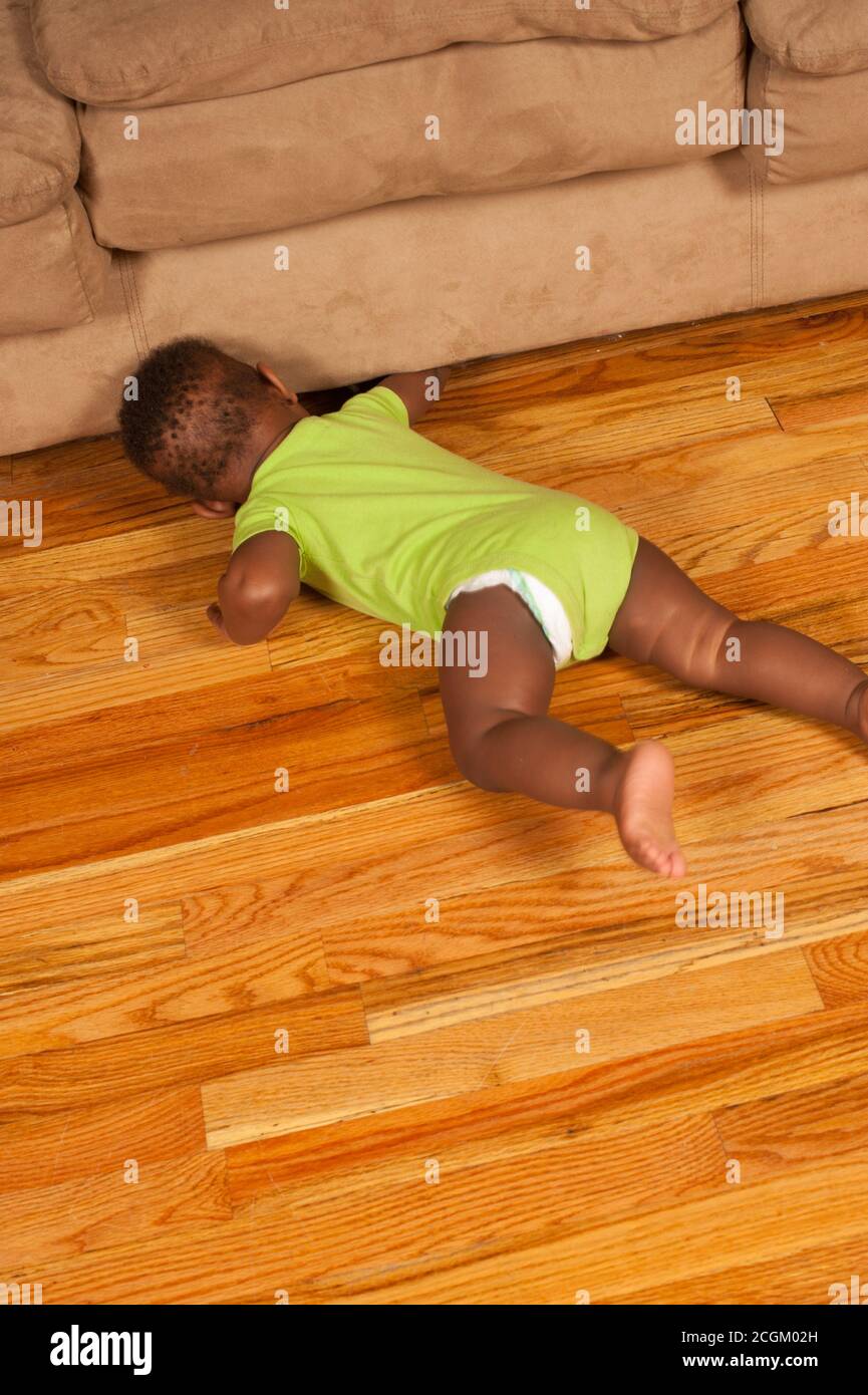 12 month old baby boy looking for toy that rolled under couch Stock Photo