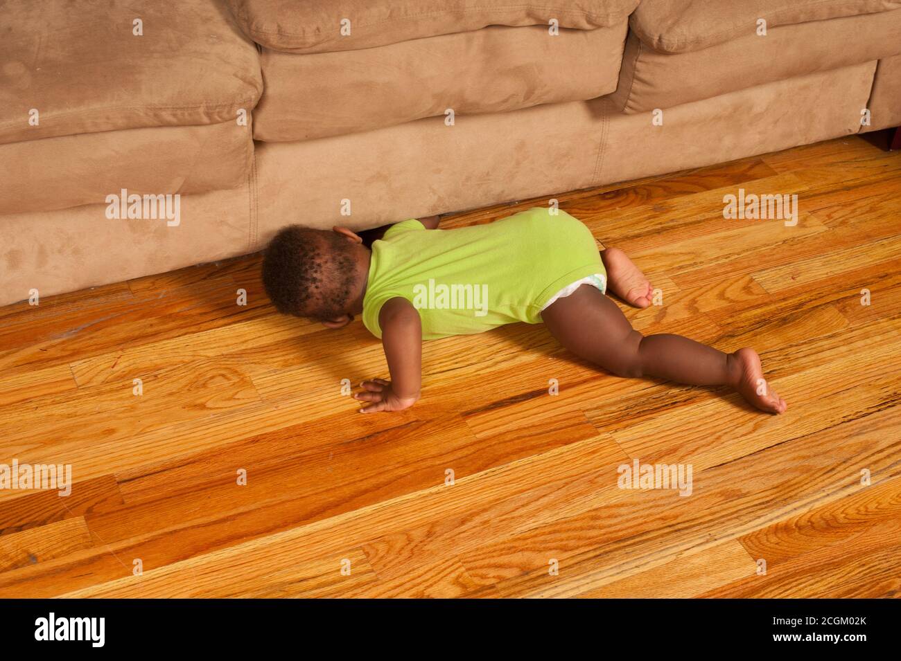 12 month old baby boy on stomach looking for toy that rolled under couch Stock Photo