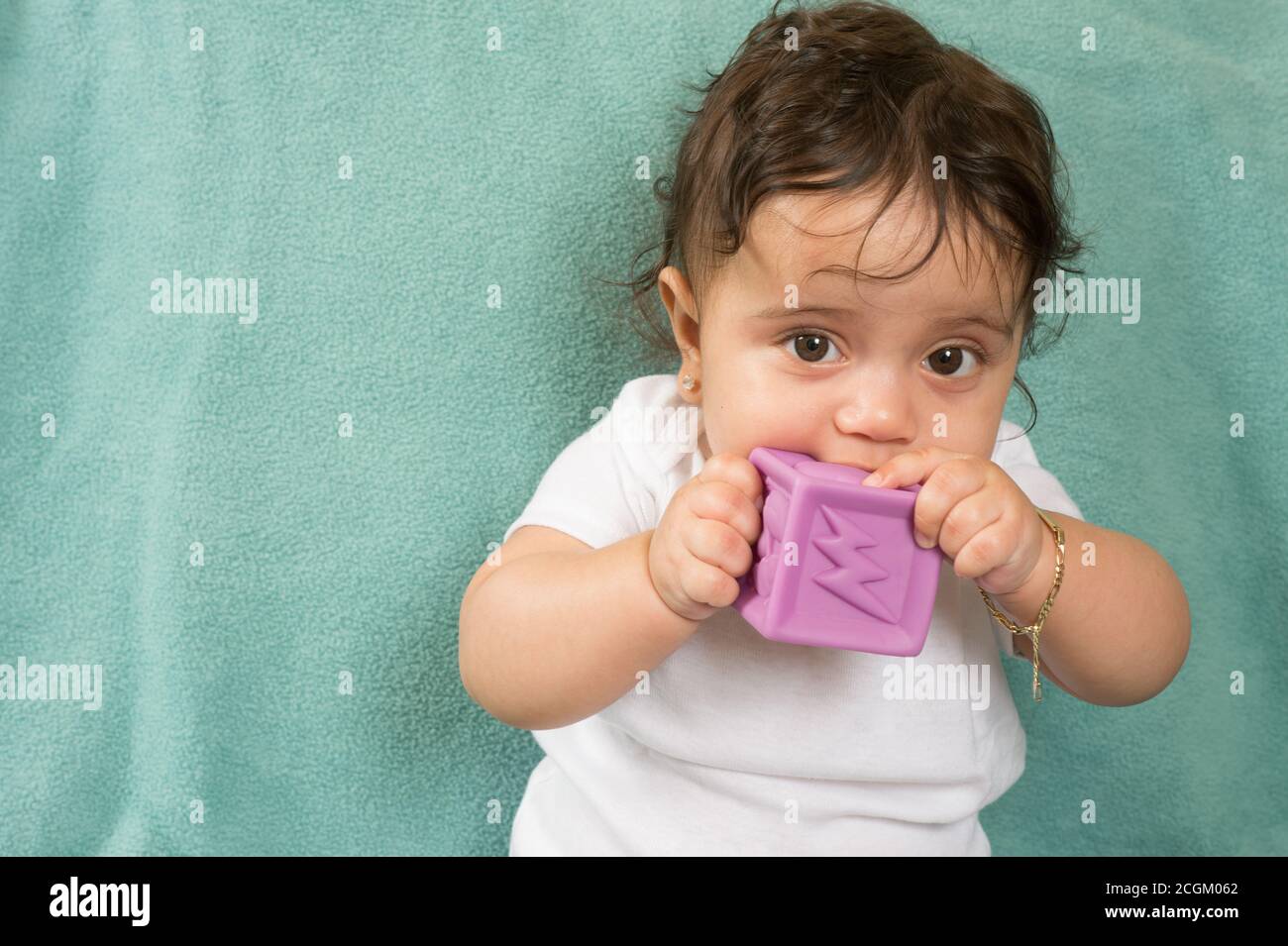 6 month old baby girl biting soft plastic block, wearing bracelet Stock Photo