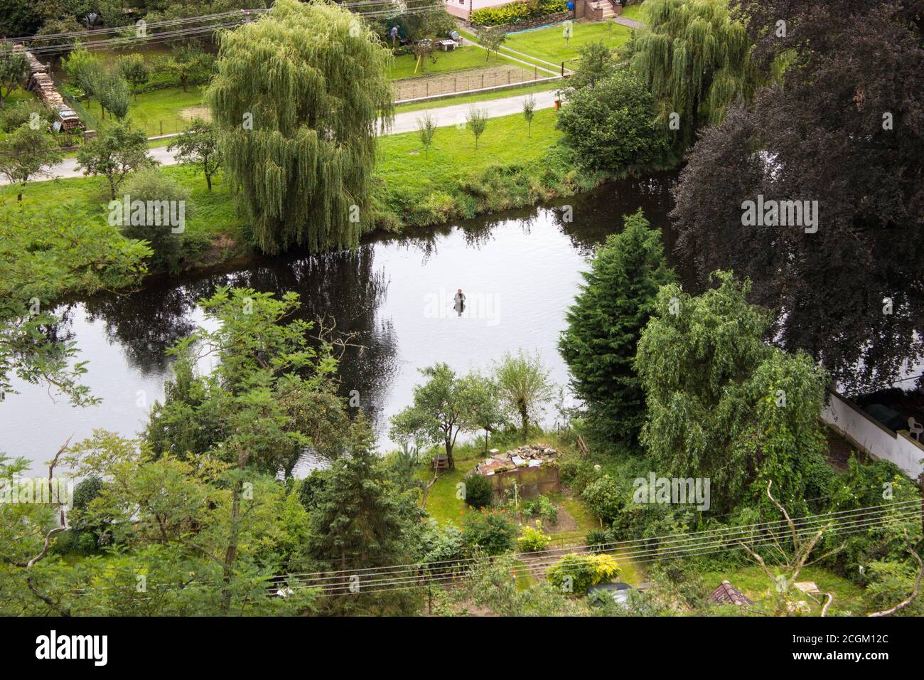 A fisherman in the river Dyje catches fish - trees, green grass, path. View from above. Reflection of trees in the water. Stock Photo