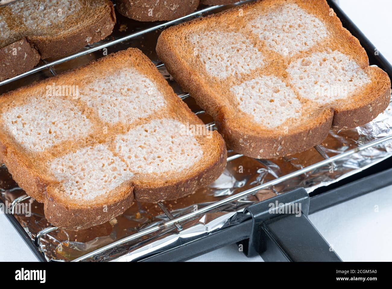 Horizontal shot of a toaster tray with four pieces of buttered wheat bread coming out of a