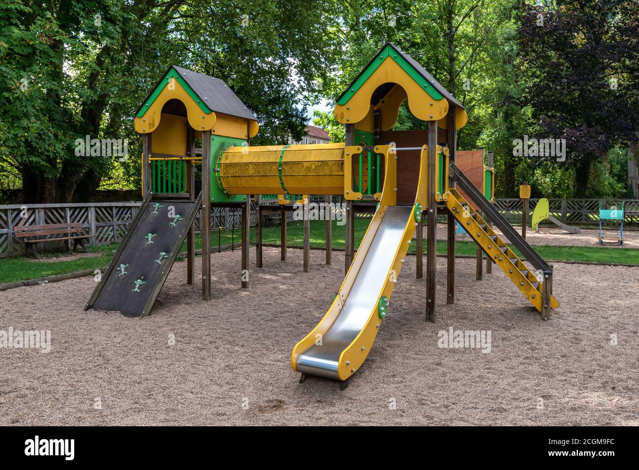 Children's playground with slide, tunnel and climbing wall in a park surrounded by trees. Stock Photo