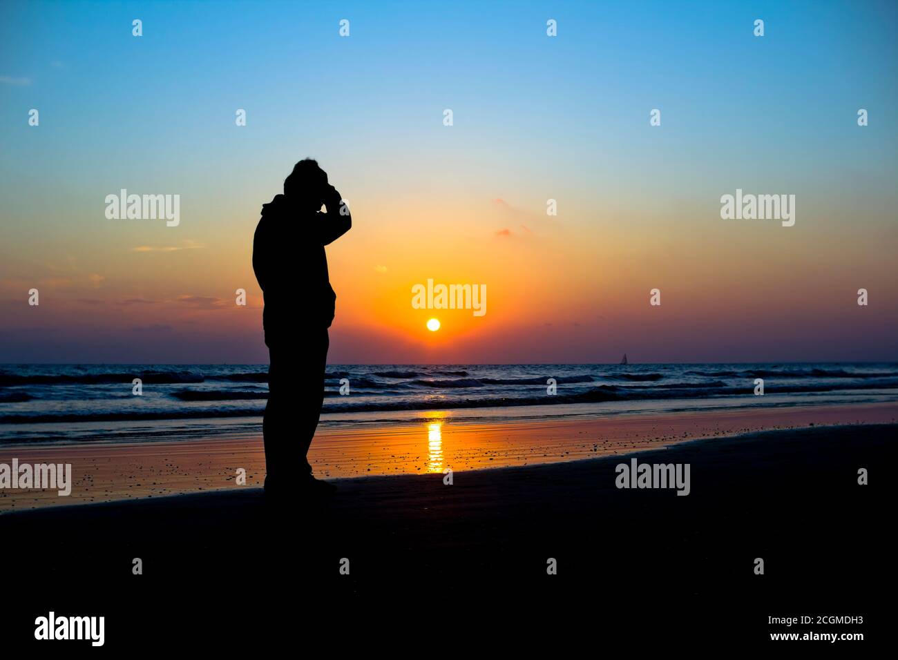 Man silhouetted against a vivid ocean sunset Stock Photo