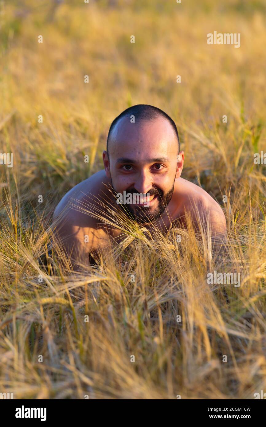 Shirtless young man concealed in a meadow smiling and looking at camera. Stock Photo