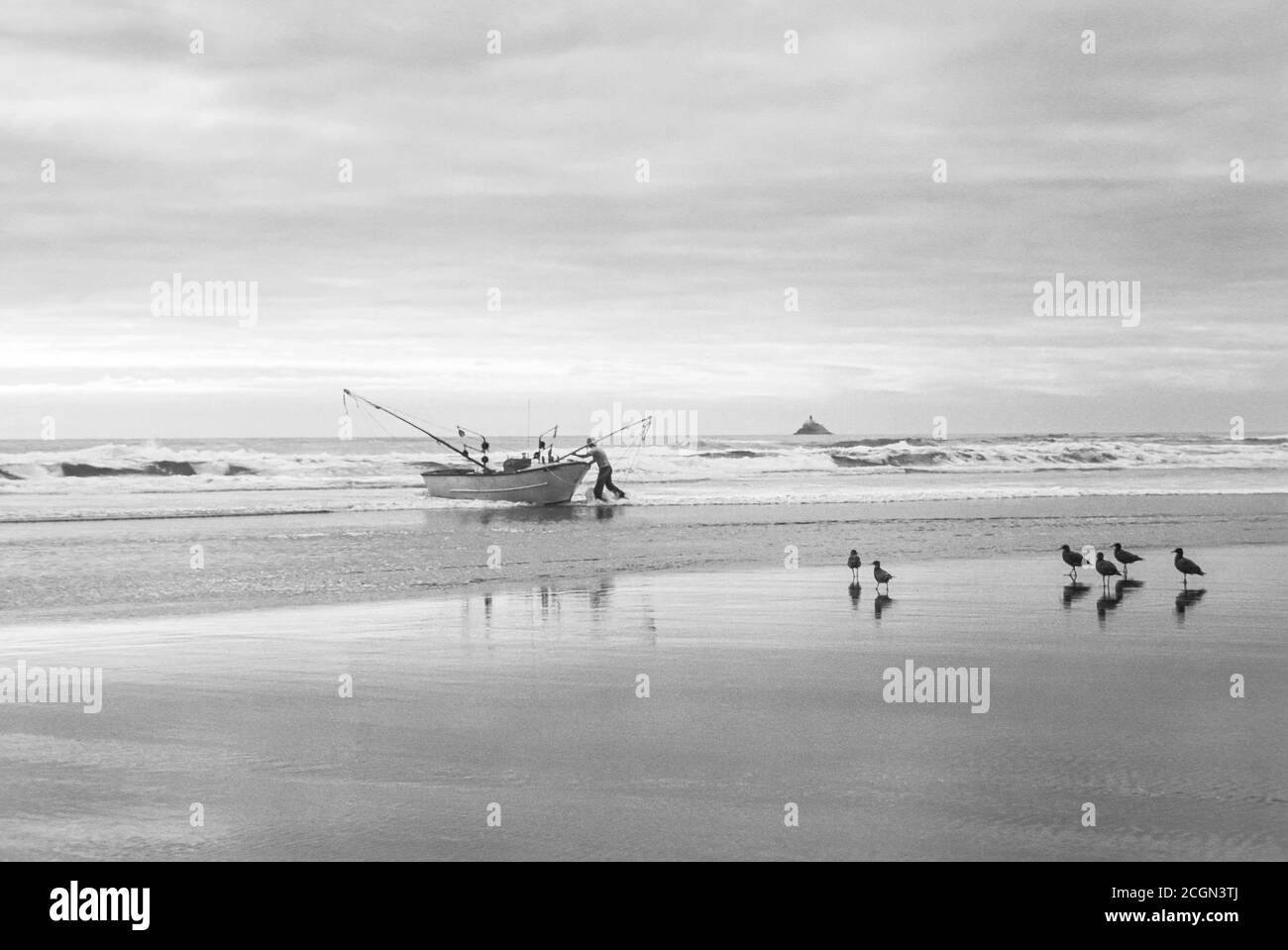 Man launching fishing dory into Pacific Ocean surf from beach at Cannon Beach, Oregon USA Stock Photo