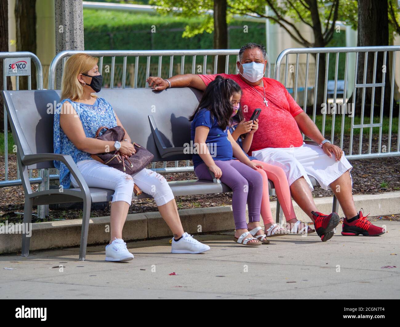 Family sitting on park bench, wearing face masks during COVID-19 pandemic. Millennium Park, Chicago, Illinois. Stock Photo